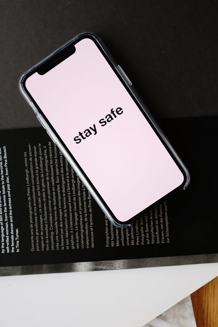 about-03 Top view of modern mobile phone with pale pink screen and STAY SAFE inscription placed on open magazine with black page and white letters during COVID 19 pandemic